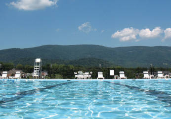 Beach chairs surround a clear swimming pool with views of the Blue Ridge Mountains behind.
